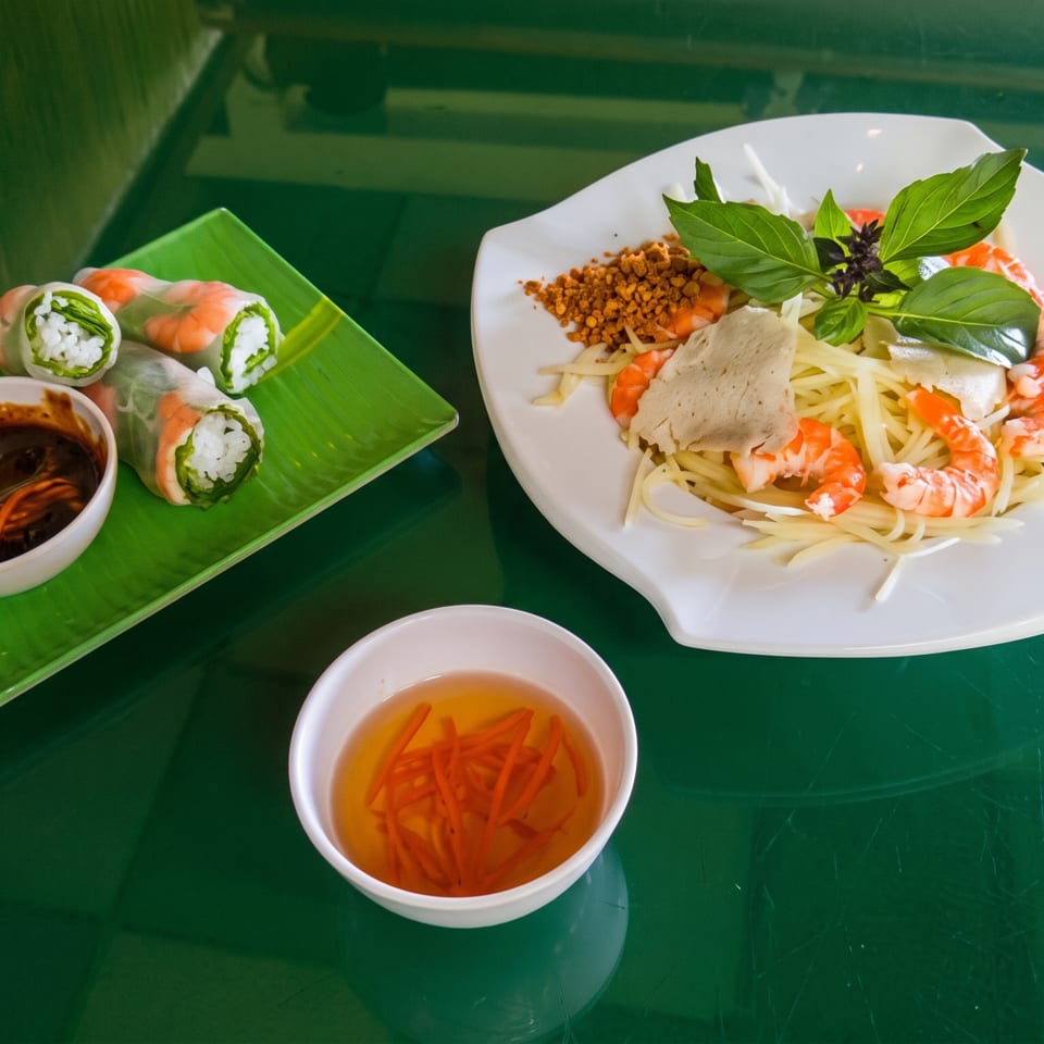 Vietnamese spring rolls with dipping sauce and a shrimp salad on a green table.