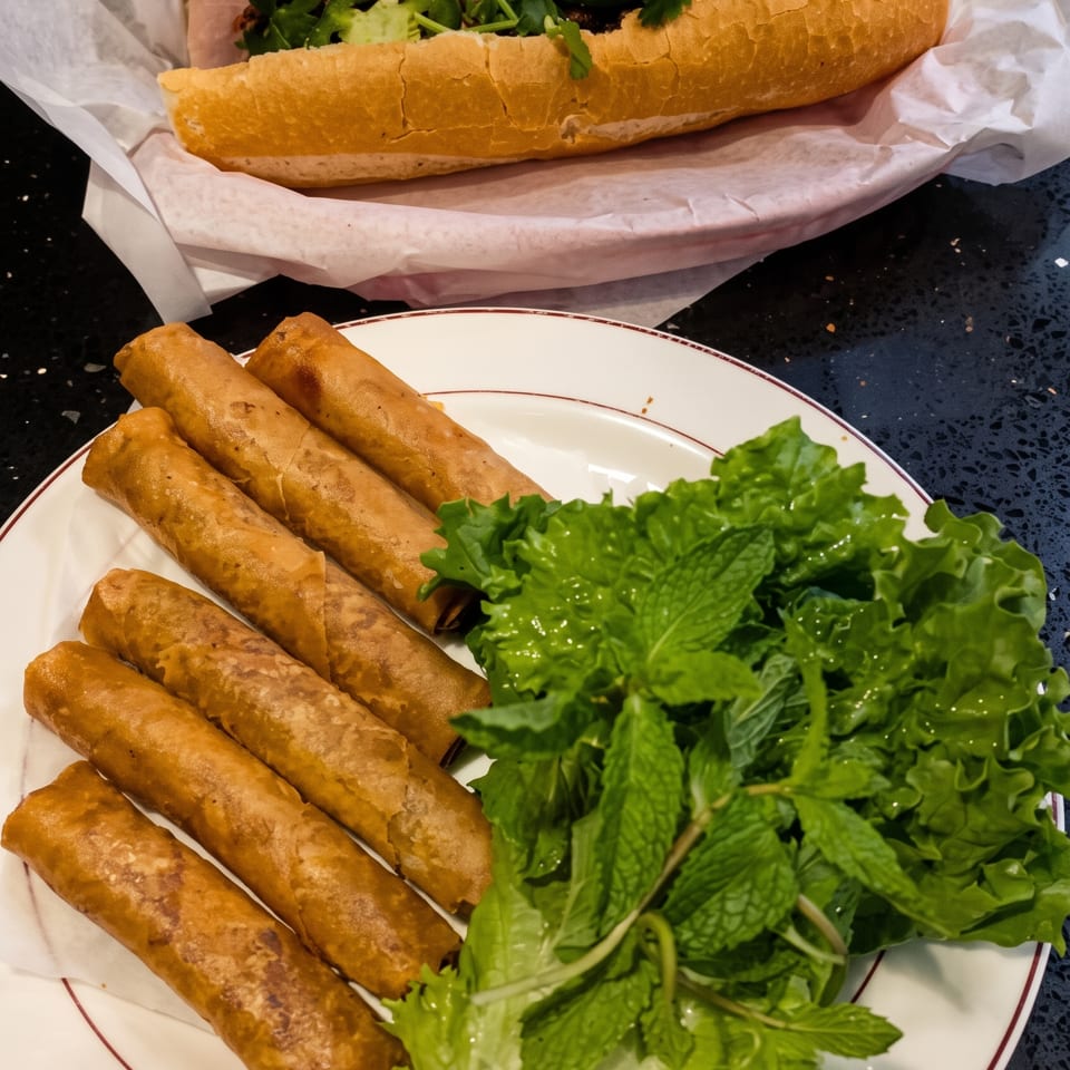 A banh mi sandwich with jalapeños and cilantro, and a plate of crispy spring rolls with lettuce and mint.