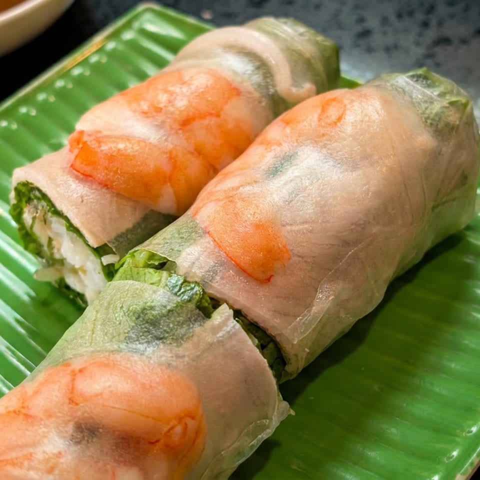 Two fresh spring rolls with shrimp and greens on a green rectangular plate.