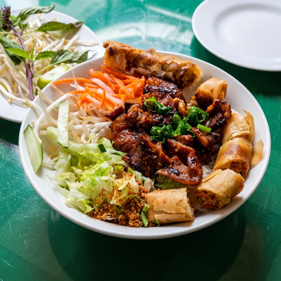 Vietnamese vermicelli bowl with grilled pork, spring rolls, and fresh vegetables on a green table.