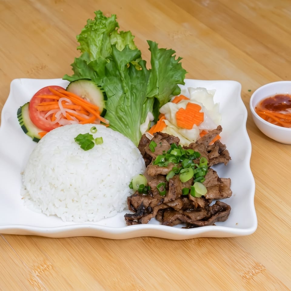 Grilled beef with rice, lettuce, cucumber, tomato, pickled carrots, and a side of dipping sauce.
