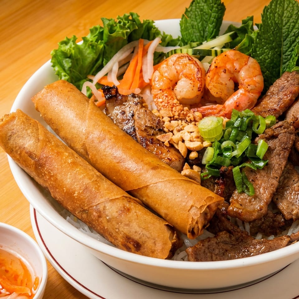 A vibrant bowl of Vietnamese vermicelli with grilled shrimp, beef, crispy spring rolls, and fresh vegetables.